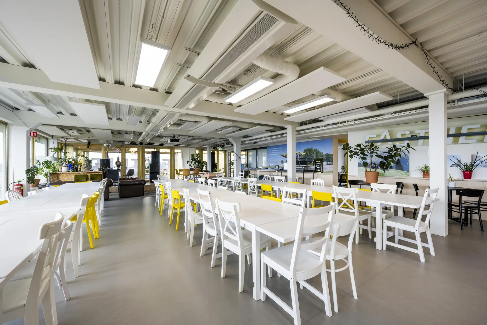 Moderne en ruime kantine met witte tafels en stoelen, gele accenten en veel planten aan de James Wattstraat.